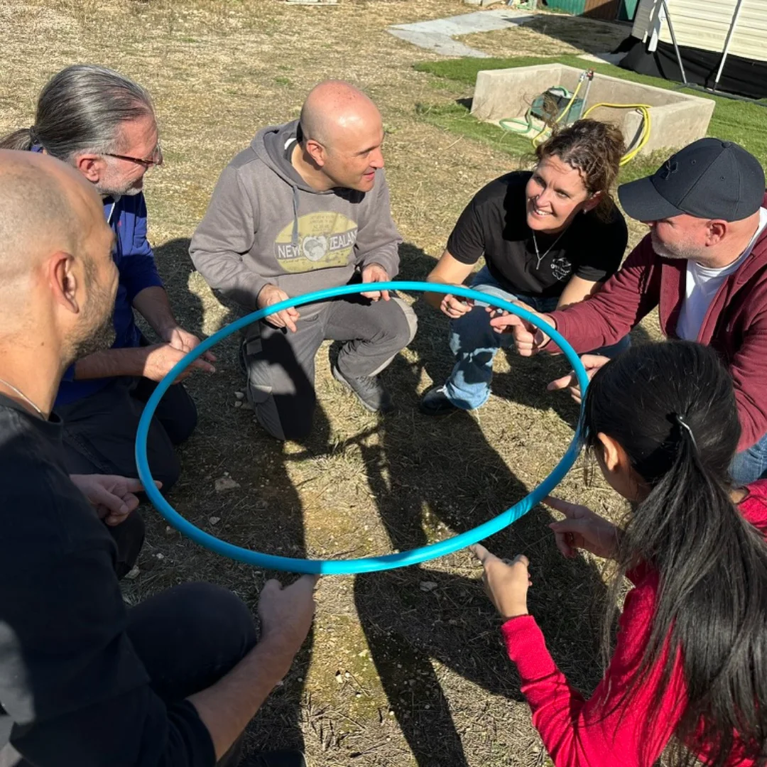 Un equipo coordina sus manos para sostener un aro durante una dinámica grupal